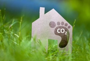 A cardboard cutout of a traditional house silhouette in green grass, with a brown footprint labeled, “CO2” on the right side to represent a carbon footprint.